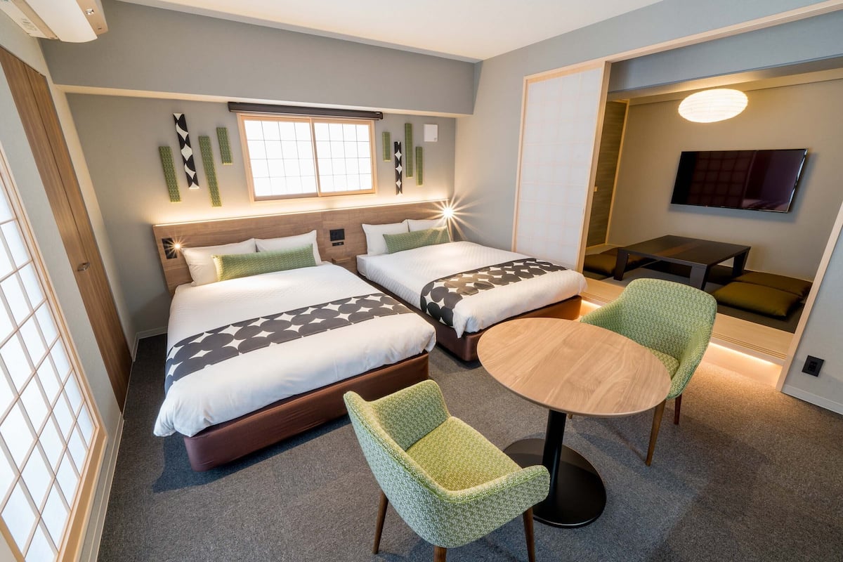 A hotel room with two beds, a small round table, and a green chair.