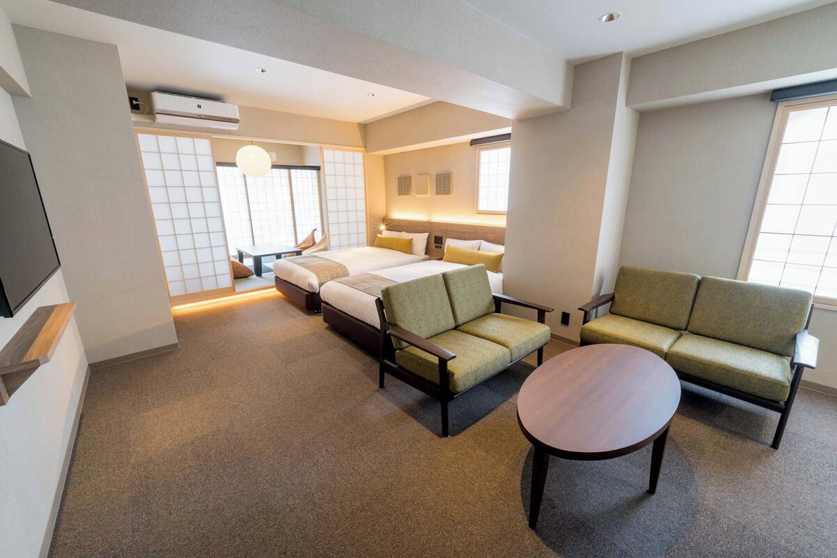 A modern hotel room with a sofa, a bed, a small table, and a TV.