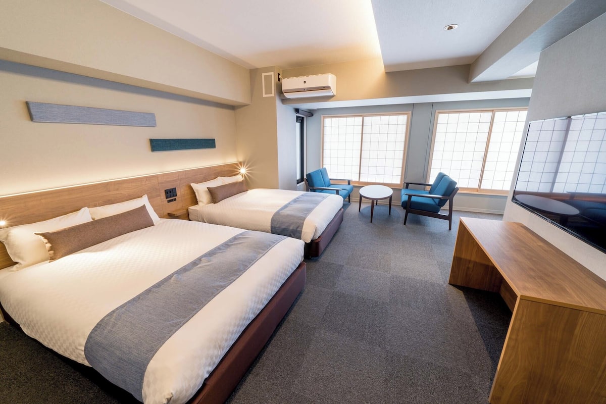 A hotel room with two beds, a desk, and a seating area with chairs.