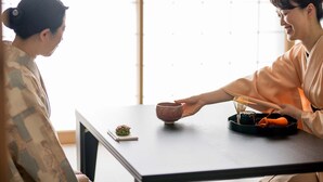 Two people seated at a table with a tea set, a small dish, and a brush. - RESI STAY HOTEL SUN CHLORELLA　 (Kyoto)