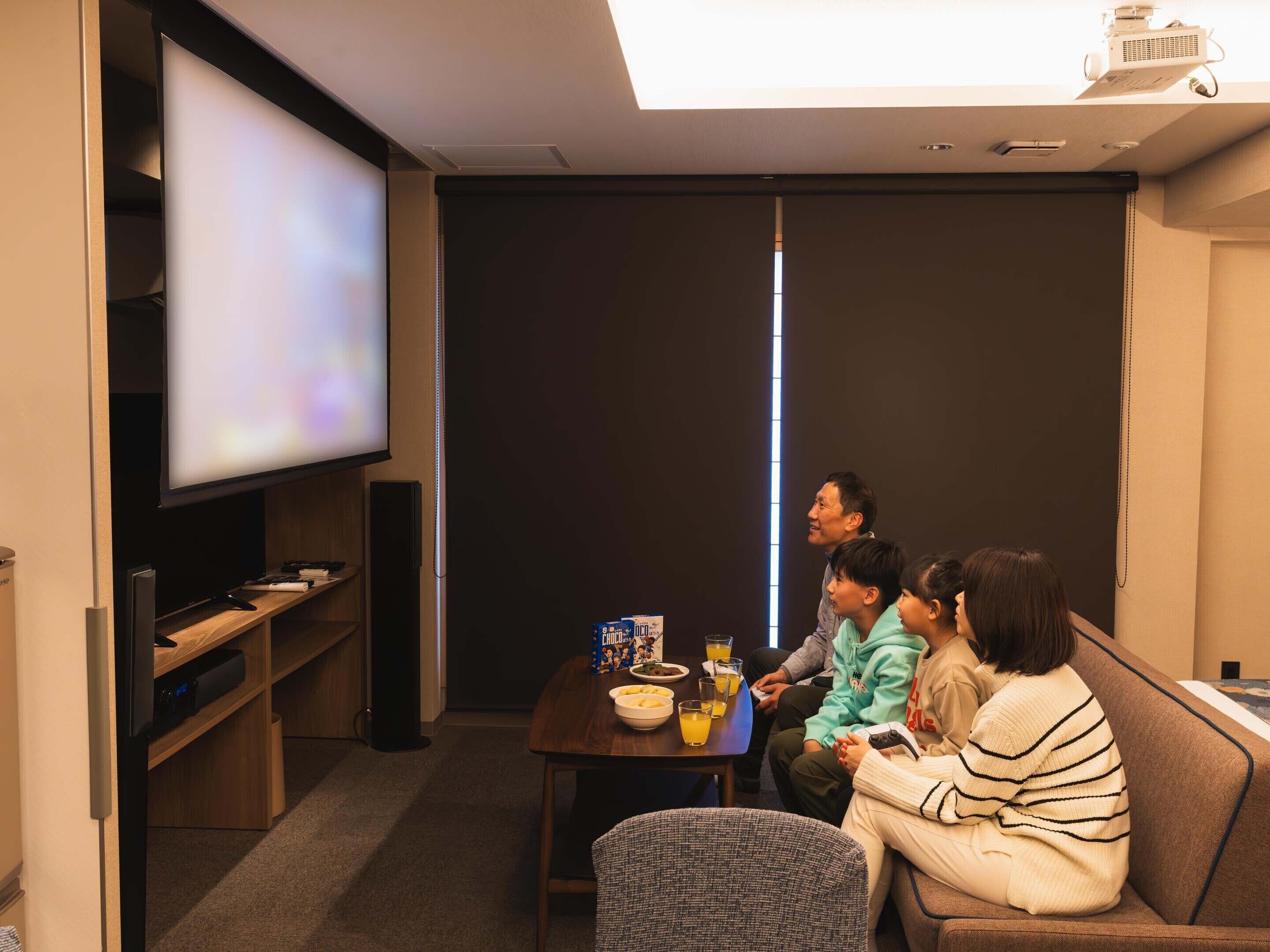A room with a large flat-screen TV, a wooden table with snacks, and a couch.