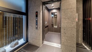 An elevator with a control panel, a glass door, and a stone wall. - RESI STAY HOTEL SUN CHLORELLA　 (Kyoto)