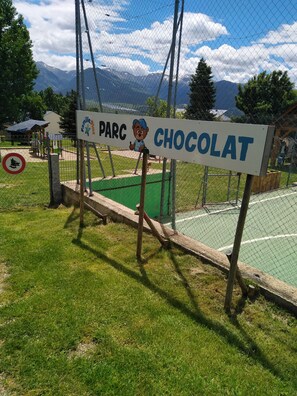 Señal de 'PARK CHOCOLAT' con un oso de caricatura, un área cercada y montañas al fondo.