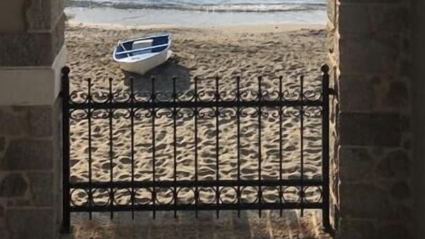 Una ventana enmarcada en piedra con vistas al mar tranquilo y un barco en la orilla.