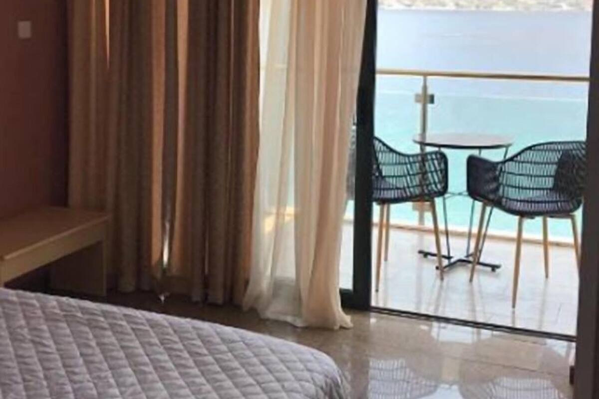 A hotel room with a bed, a balcony with a table and chairs, and a view of the sea.