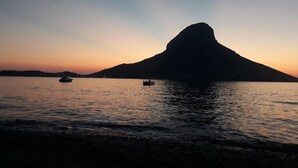 Silueta de una montaña al atardecer sobre un cuerpo de agua tranquilo, con barcos.