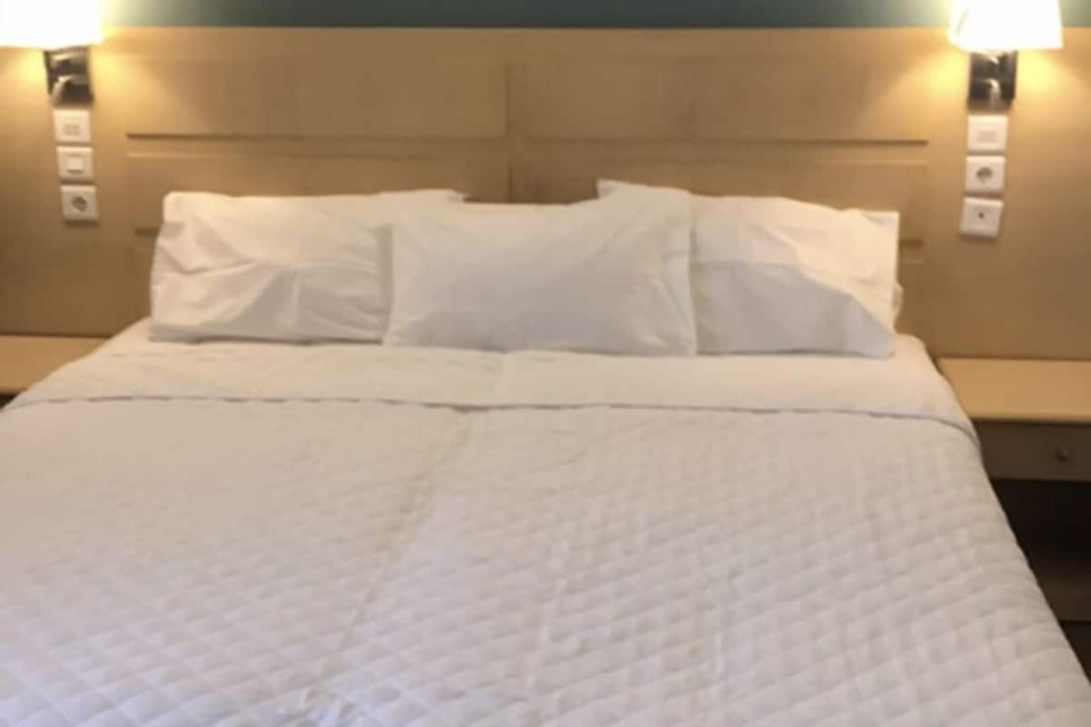 A neatly made bed with white bedding and a quilted duvet, flanked by two wall-mounted lamps on either side.