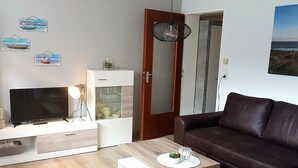 Una sala de estar moderna con un sofá de cuero marrón, una mesa de centro de madera, un televisor sobre un mueble blanco y piso de madera.