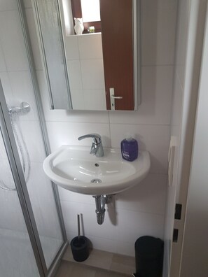 Une salle de bain avec un lavabo blanc, un miroir au-dessus, une porte de douche et des toilettes.