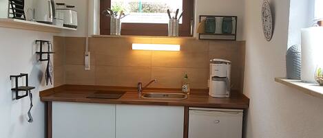A compact kitchen with a wooden countertop, a sink, a window with a view, a dining table with chairs, and a trash bin.