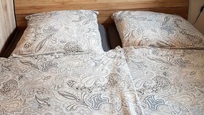Una cama doble con ropa de cama estampada, un cabecero de madera y un cuadro de un muelle al atardecer en la pared.