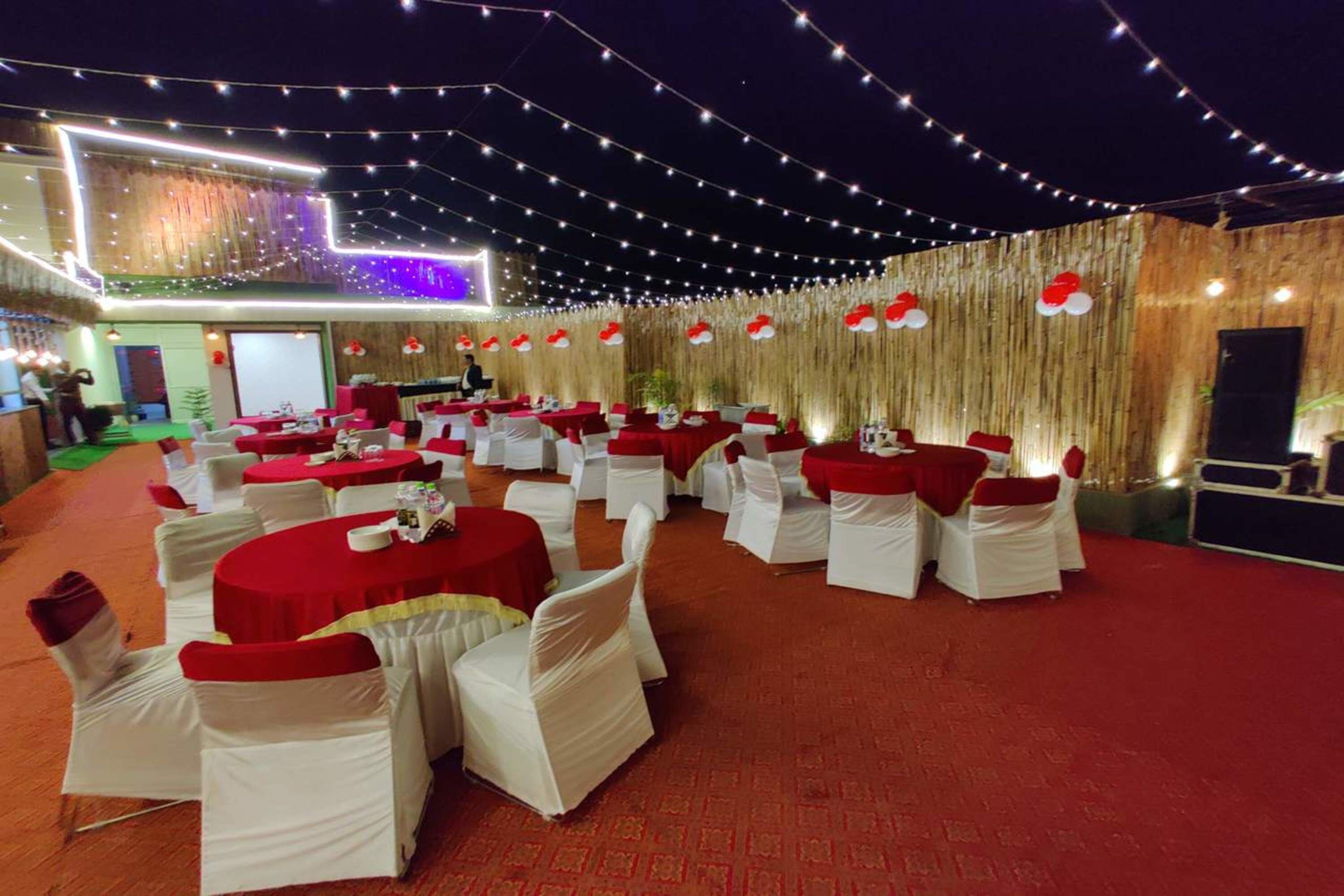 A banquet hall with round tables and white chairs, decorated with red tablecloths and white chair covers.