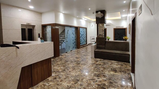 A modern reception area with a marble floor, a reception desk, a staircase, and a sign that reads "MIDAS". - La Imperio Hotel (Aligarh)