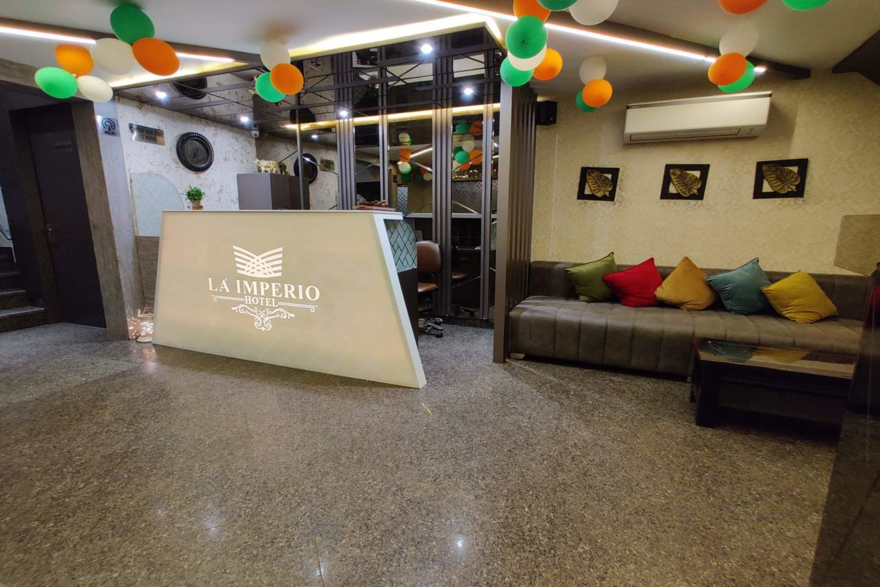 A reception area with a reception desk labeled "LA IMPERIO HOTEL," a sofa with colorful cushions, and a wall-mounted air conditioner.