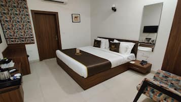 A well-lit hotel room with a large bed, a bedside table, a chair, a wardrobe, and a mirror.