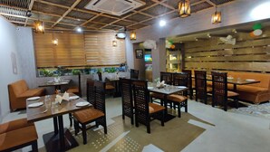 A restaurant with wooden ceiling, tables, chairs, and a wall with shelves. - La Imperio Hotel (Aligarh)
