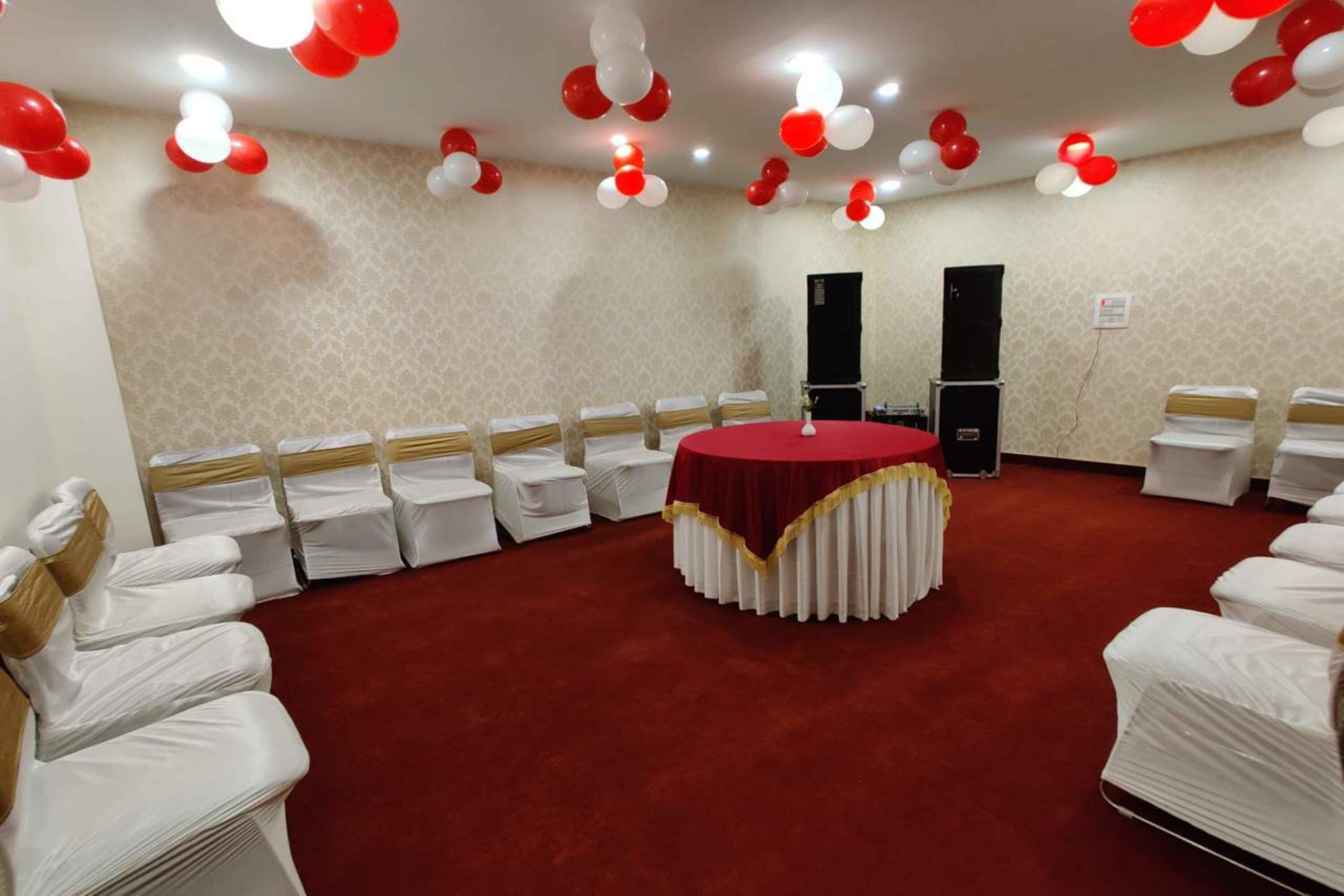 A conference room with white chairs arranged in rows, a central round table with a red tablecloth, and red and white balloons on the ceiling.