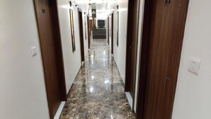 A long, narrow hallway with marble flooring and wooden doors, each marked with a number. - La Imperio Hotel (Aligarh)