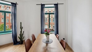 Ein Essbereich mit einem Holztisch, sechs Stühlen, einer Vase mit Blumen und zwei mit Vorhängen versehenen Fenstern.