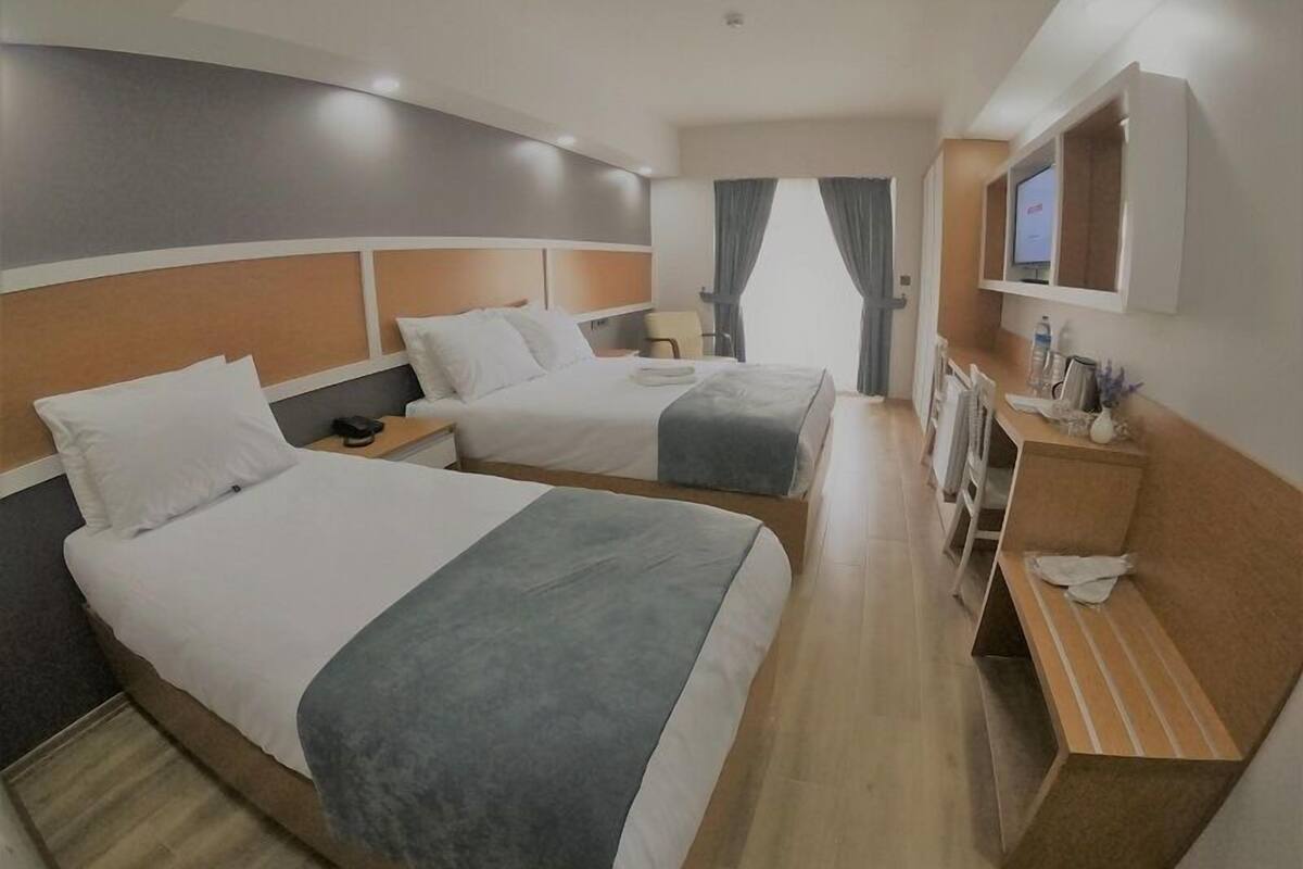 A hotel room with two beds, a desk, a TV, and a window with curtains.