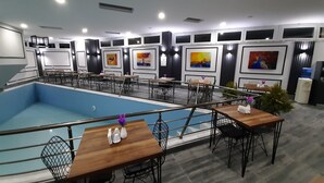 A modern indoor pool area with multiple tables and chairs, surrounded by walls decorated with framed artwork. - Asiwa Otel (Eskisehir)