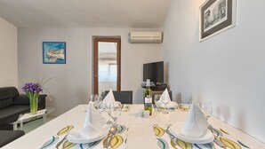 Un comedor con una mesa dispuesta para dos personas, un jarrón con flores moradas y un cuadro en la pared.