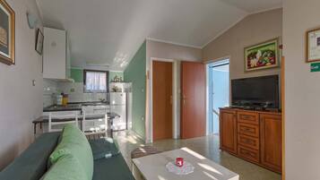 Un espacio habitable compacto con kitchenette, zona de comedor y sala de estar con televisor.