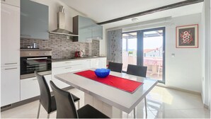 Una cocina moderna con armarios blancos, horno empotrado y un mantel rojo en la mesa de comedor.