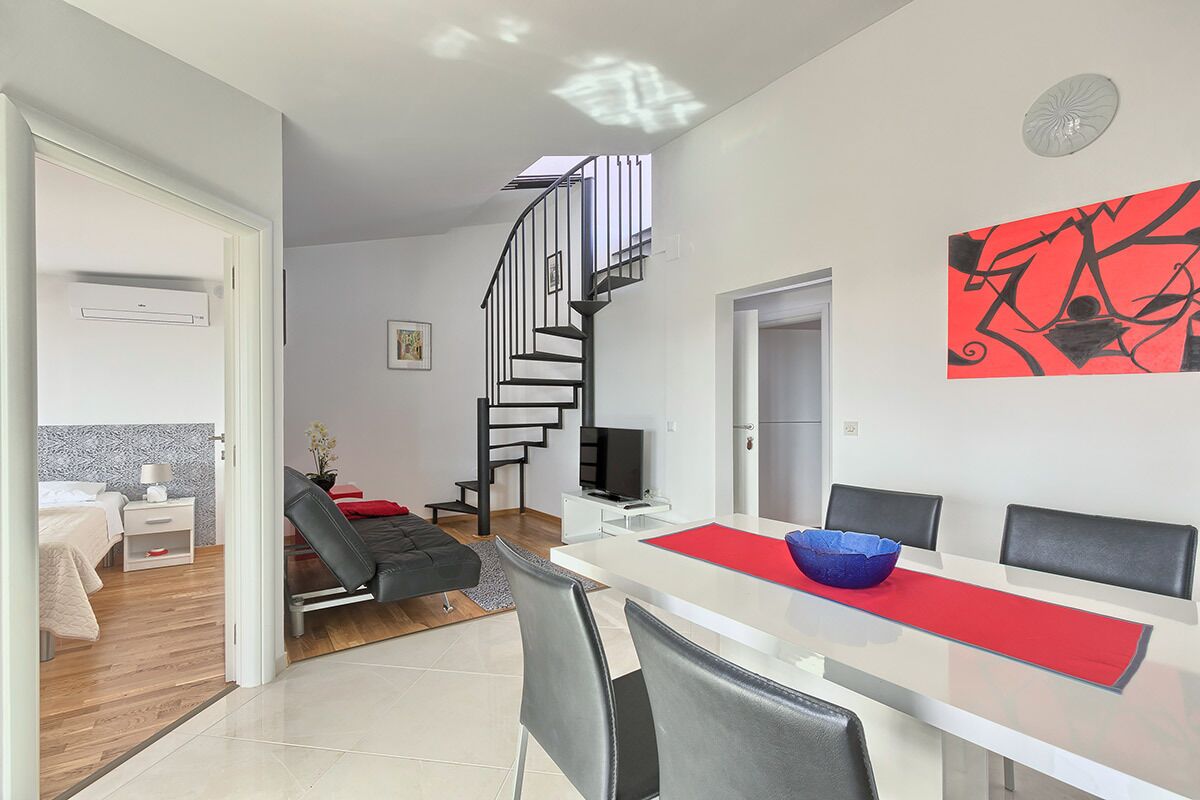 A modern living room with a dining area, a staircase, and a red abstract painting.