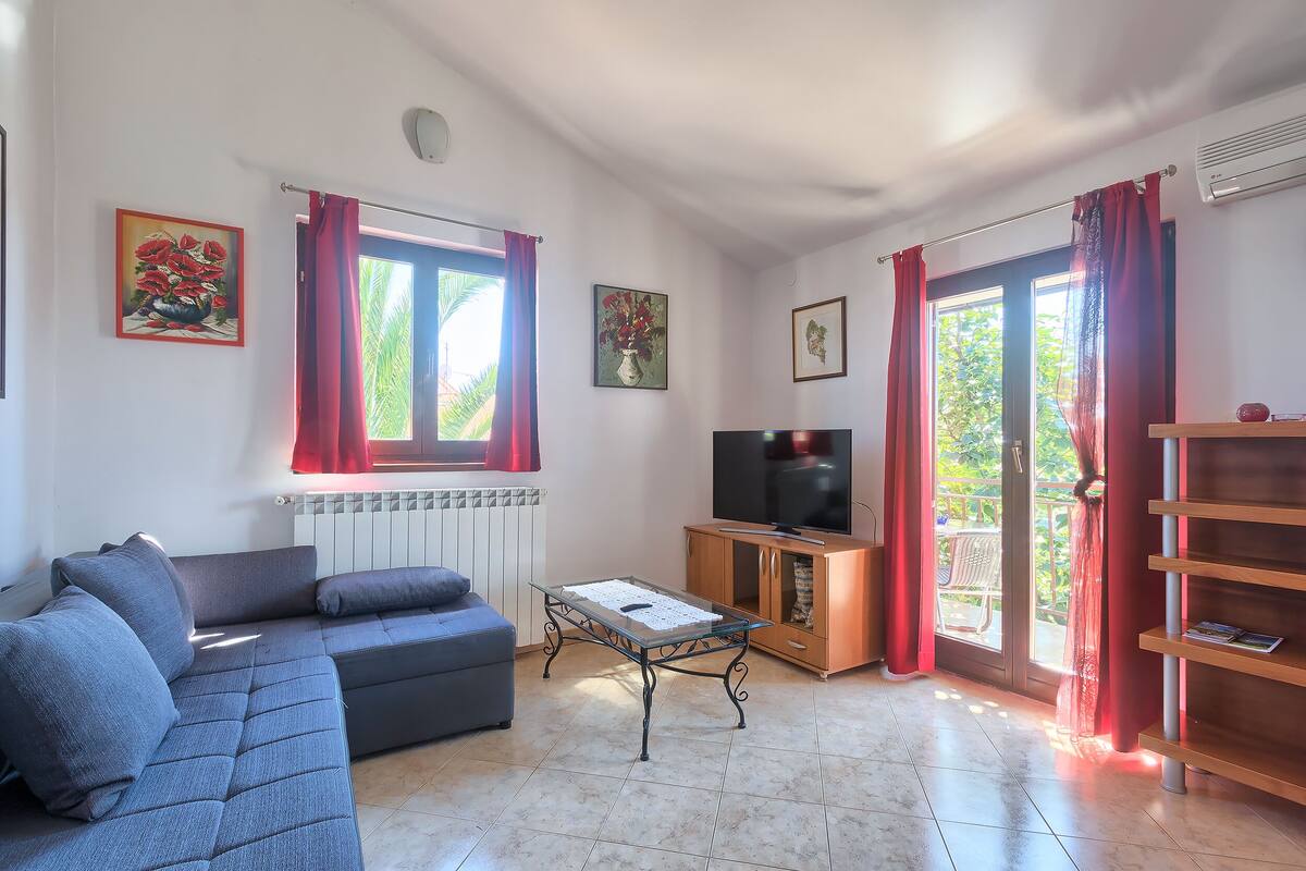Una sala de estar con un sofá, una mesa de centro, un televisor y un ventanal corredizo que da a un espacio exterior.