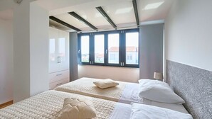 Un dormitorio con dos camas, un armario y una ventana con vistas a edificios.