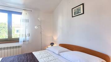 A bedroom with a bed, a window with curtains, a bedside lamp, and a framed picture on the wall.