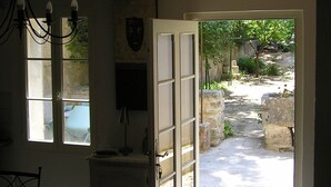 Puerta abierta que da a un patio con muro de piedra y vegetación.