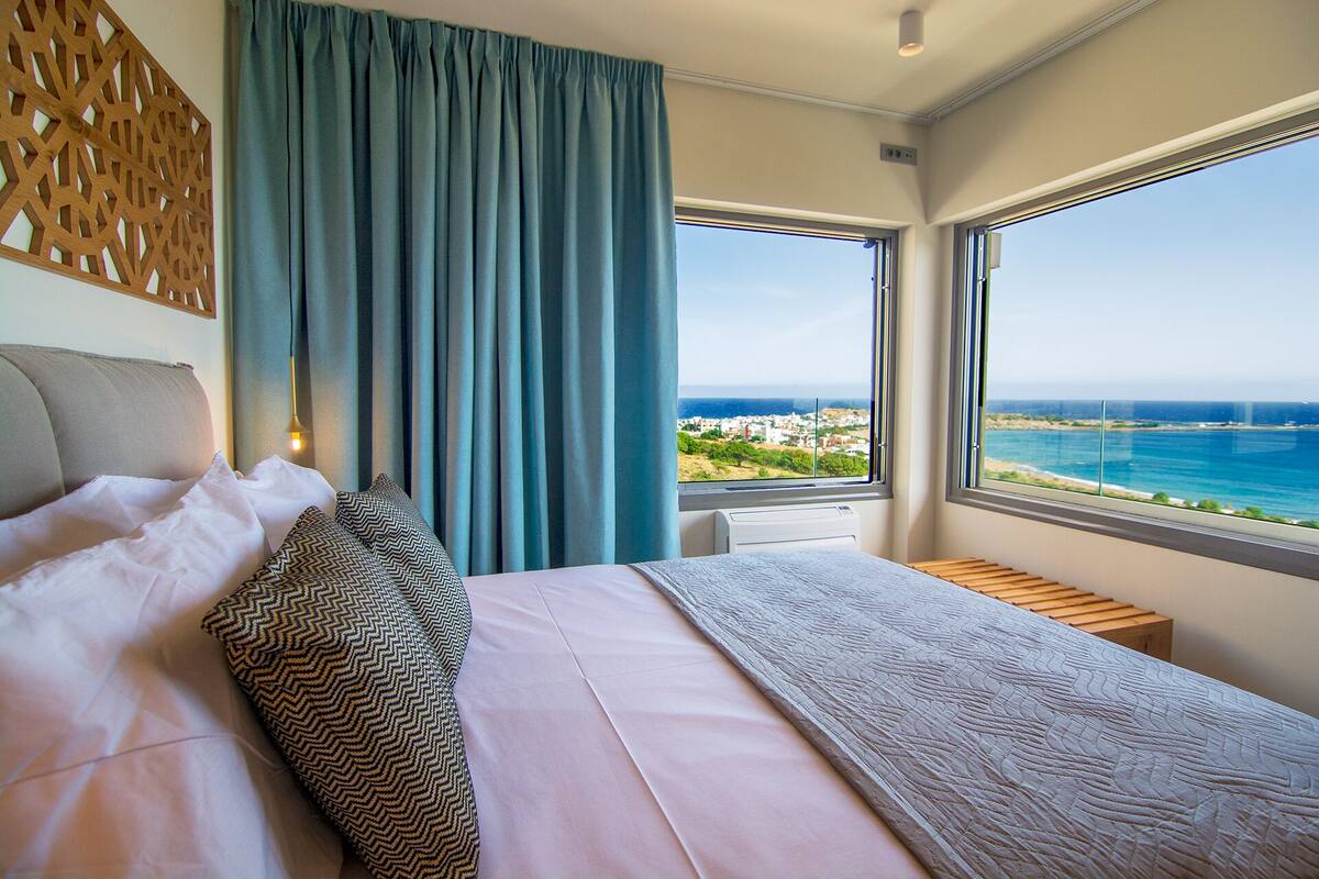 A bedroom with a large bed, a view of the sea, and a wooden partition.