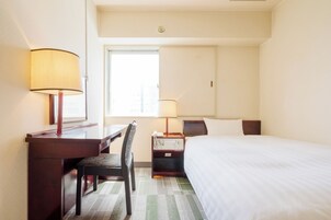 Habitación de hotel con cama, escritorio, silla, dos lámparas de noche y ventana.