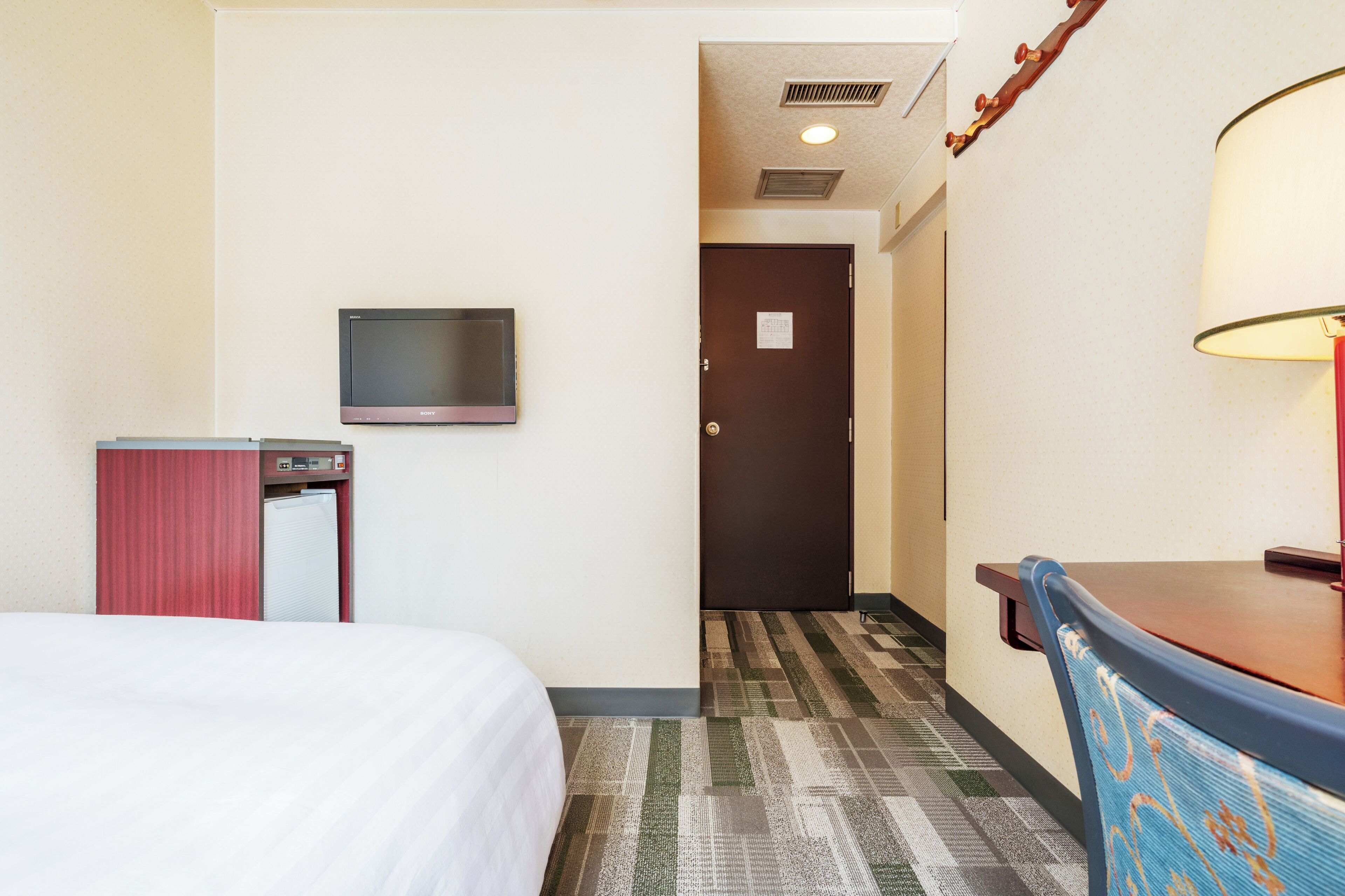 A hotel room with a bed, a desk, a television, and a door leading to another room.