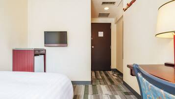 A hotel room with a bed, a desk, a television, and a door leading to another room.