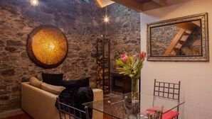 Um quarto acolhedor com parede de pedra, luminária redonda, lareira, mesa de vidro com cadeiras e um espelho emoldurado.