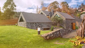 Uma casa de pedra com telhado inclinado, um caminho de pedras que leva à entrada e um gramado.