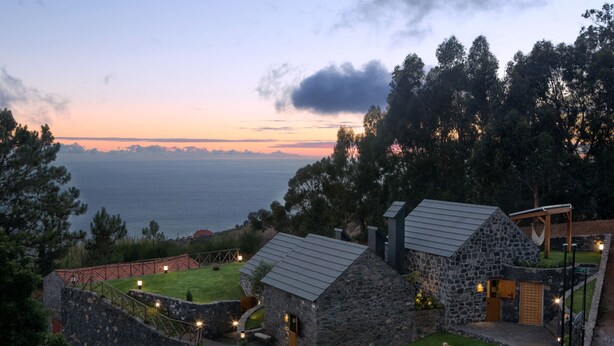Um edifício de pedra com telhado de metal, rodeado por uma cerca de madeira e uma área ajardinada.