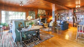 A cozy cabin interior with a wooden ceiling, a fireplace, a sofa, a dining table, and a bookshelf. - The Historic Northern Hotel (Coolin)