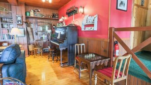 A cozy room with wooden floors, a piano, a chess table, and a red wall with various items and a framed picture. - The Historic Northern Hotel (Coolin)