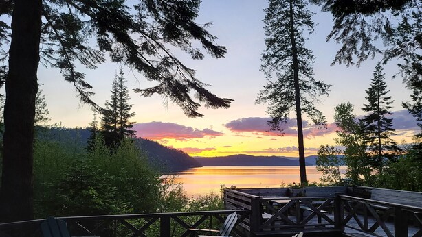 A wooden deck with Adirondack chairs and a table, overlooking a lake with a sunset view. - The Historic Northern Hotel (Coolin)