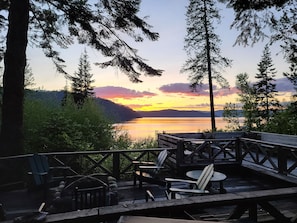 A wooden deck with Adirondack chairs and a table, overlooking a lake with a sunset view. - The Historic Northern Hotel (Coolin)