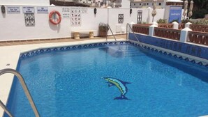 Una piscina con un adhesivo de delfín, rodeada por un suelo de baldosas y una pared blanca con señales de seguridad.
