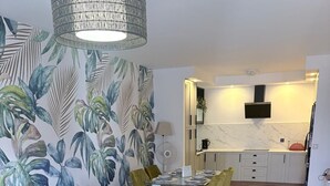 Una sala de estar moderna con un sofá, una mesa de comedor y sillas. Cuenta con una zona de cocina con encimera de mármol y un televisor de pantalla plana montado en la pared.