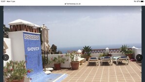 Terraza en la azotea con una zona de ducha azul, plantas en macetas y sillones de descanso.