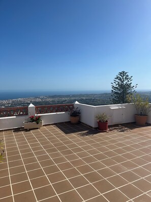 A rooftop terrace with tiled flooring, potted plants, and a view of a cityscape and coastline.