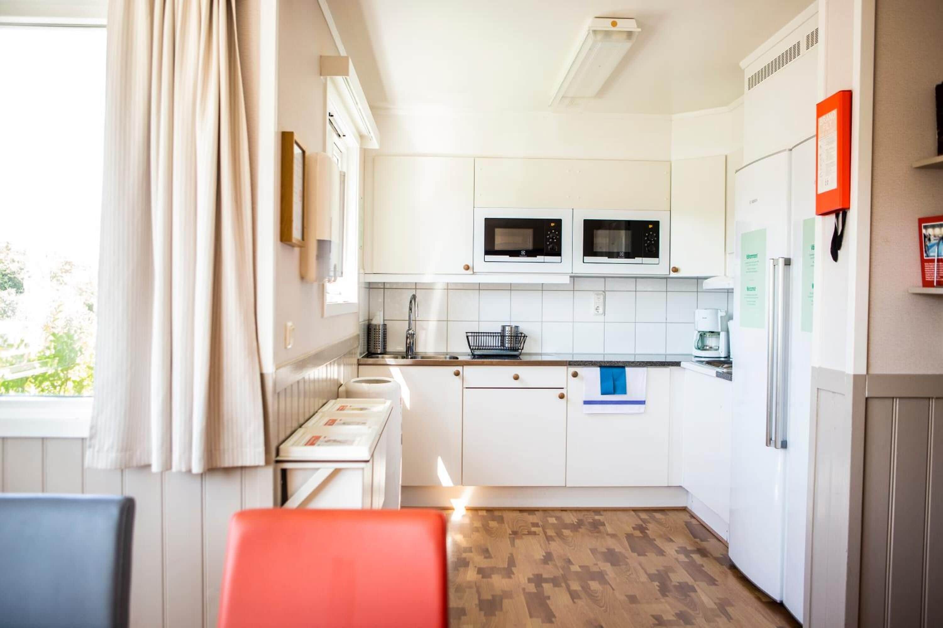 Cocina compacta con armarios blancos, dos microondas empotrados, cafetera y refrigerador.