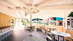 Un café en plein air avec de nombreuses tables et des bancs, une colonne centrale et un espace dédié aux distributeurs automatiques.